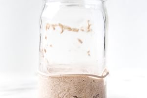 Bubbly sourdough starter in a glass jar with visible rise and fermentation bubbles along the sides.
