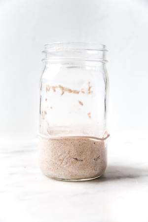 Bubbly sourdough starter in a glass jar with visible rise and fermentation bubbles along the sides.