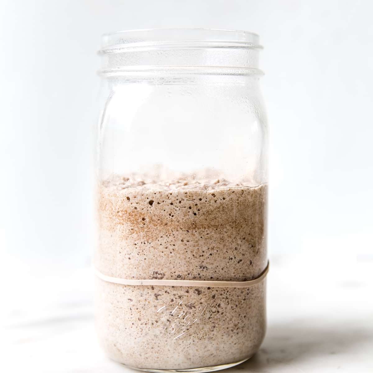 Bubbly sourdough starter in a glass jar with visible rise and fermentation bubbles along the sides.