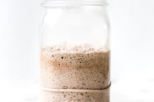 Bubbly sourdough starter in a glass jar with visible rise and fermentation bubbles along the sides.
