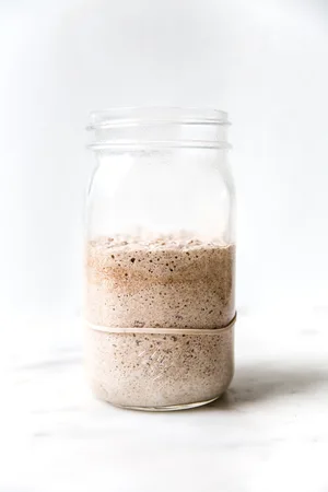 Bubbly sourdough starter in a glass jar with visible rise and fermentation bubbles along the sides.