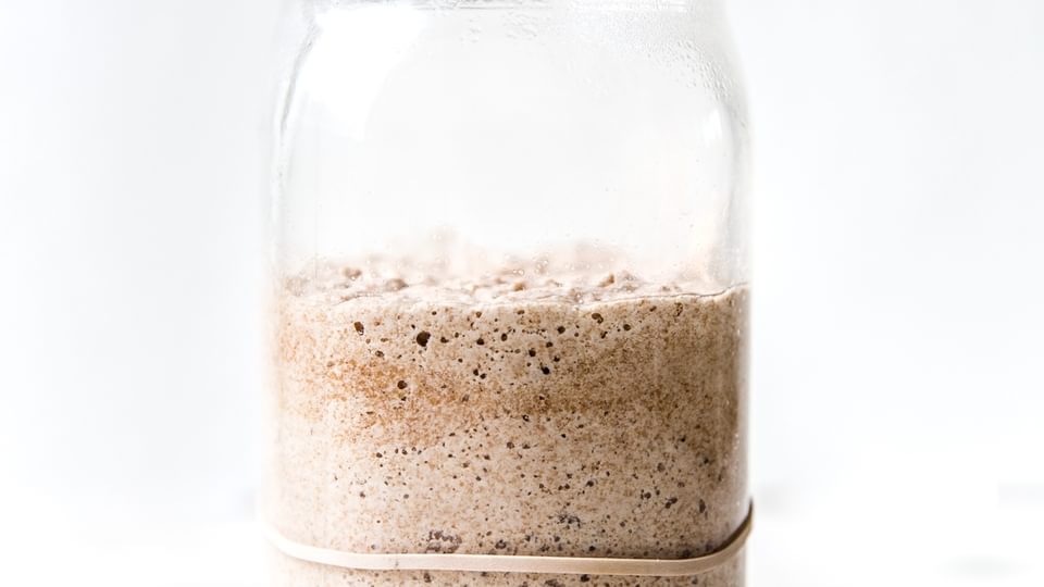 Bubbly sourdough starter in a glass jar with visible rise and fermentation bubbles along the sides.