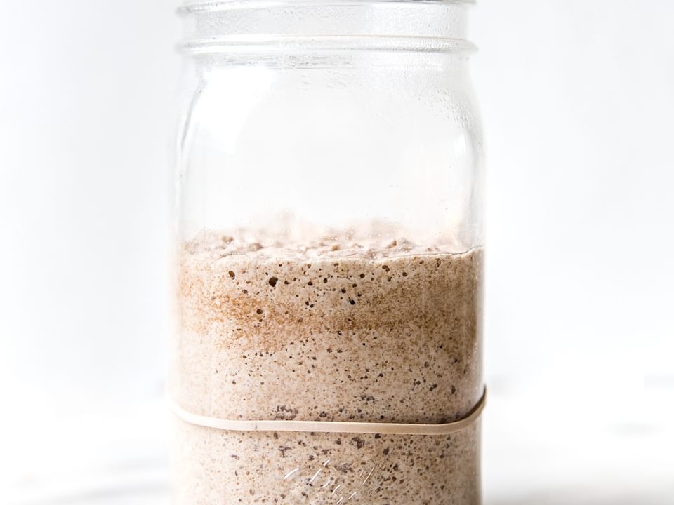 Bubbly sourdough starter in a glass jar with visible rise and fermentation bubbles along the sides.