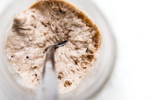 Bubbly sourdough starter in a glass jar with visible rise and fermentation bubbles along the sides.