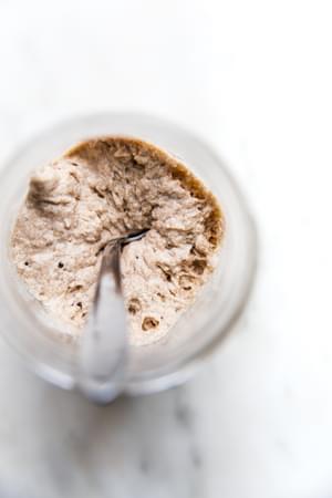 Bubbly sourdough starter in a glass jar with visible rise and fermentation bubbles along the sides.
