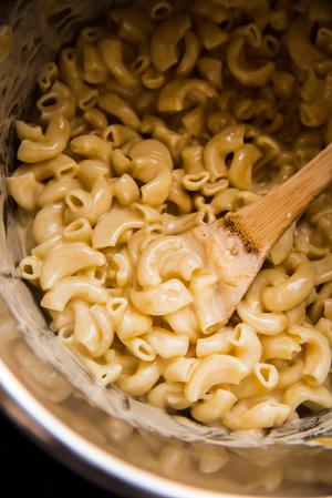 Instant pot mac and cheese with cheddar cheese, parmesan cheese and heavy cream being stirred with a wooden spoon