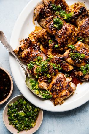 lemongrass chicken thighs with scallion oil and a sriracha-brown sugar sauce on a plate with a spoon