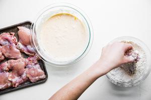 Hands shown dipping buttermilk fried chicken into a bowl of spiced flour mixture.