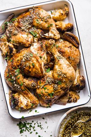 zaatar chicken sheetpan dinner with caulilfower and shallots on a white baking dish next to za'atar oil