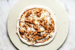 pizza dough topped with grated cheese, bbq sauce and shredded chicken.