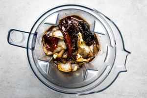 a blender filled with birria sauce ingredients, including dried red chilies, onion, spices, beef broth and white vinegar