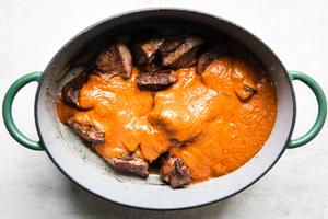 Browned chuck roast in a large pot, generously covered with rich, red birria sauce, ready to be slow-cooked