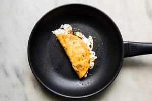 A birria taco being fried in a skillet, with crispy edges forming on the tortilla and rich, red consommé seeping out