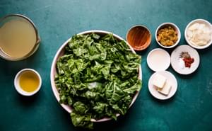 greens, olive oil, chicken stock, garlic cloves, maple syrup, golden raisins, and spices in bowls on the counter
