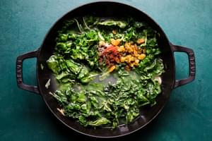 ingredients for braised greens with golden raisins and maple cooking in a skillet