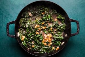 ingredients for braised greens with golden raisins and maple cooking in a skillet