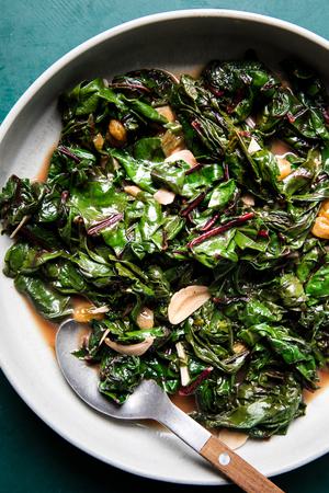 Braised Greens with Golden Raisins and Maple in a serving dish with a serving spoon