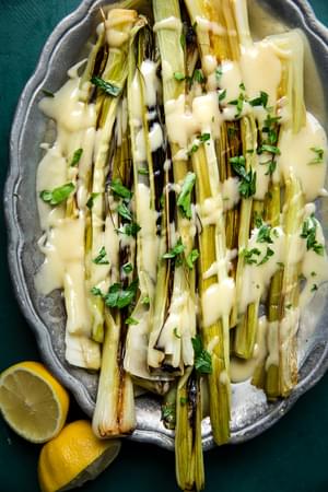 Braised Leeks with Beurre Blanc (French Butter Sauce) on a serving platter with a halved lemon beside it