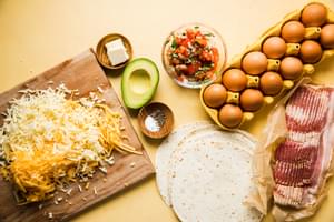 eggs, bacon, flour tortillas, pico de Gallo, avocado, butter, salt and pepper on the counter for making breakfast quesadillas