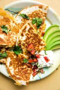 a breakfast quesadilla filled with cheese, bacon, eggs and pico de Gallo on a plate with avocado and sour cream