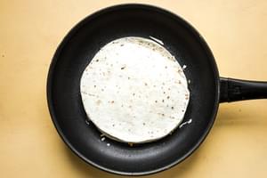 a breakfast quesadilla in a skillet filled with scrambled eggs, pico de Gallo, bacon and cheese