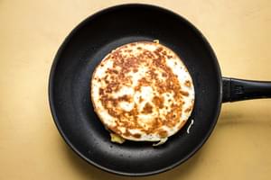 a breakfast quesadilla in a skillet filled with scrambled eggs, pico de Gallo, bacon and cheese