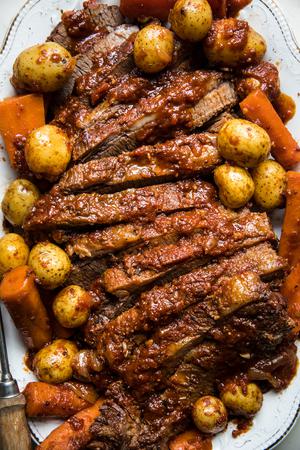 homemade braised brisket sliced on a serving platter nestled with carrots and potatoes
