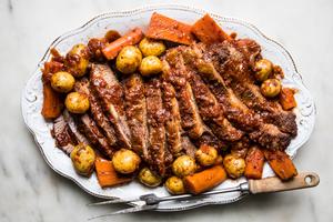 homemade braised brisket sliced on a serving platter nestled with carrots and potatoes