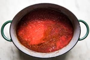 garlic, whole grain mustard, tomato paste, red wine and canned tomatoes being cooked in a dutch oven