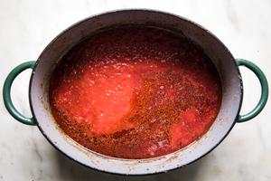 garlic, whole grain mustard, tomato paste, red wine and canned tomatoes being cooked in a dutch oven