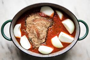 Braised brisket and onions nestled in sauce in a dutch oven