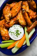 Plate of baked buffalo chicken wings served with fresh celery sticks, carrot sticks, and blue cheese dressing for dipping