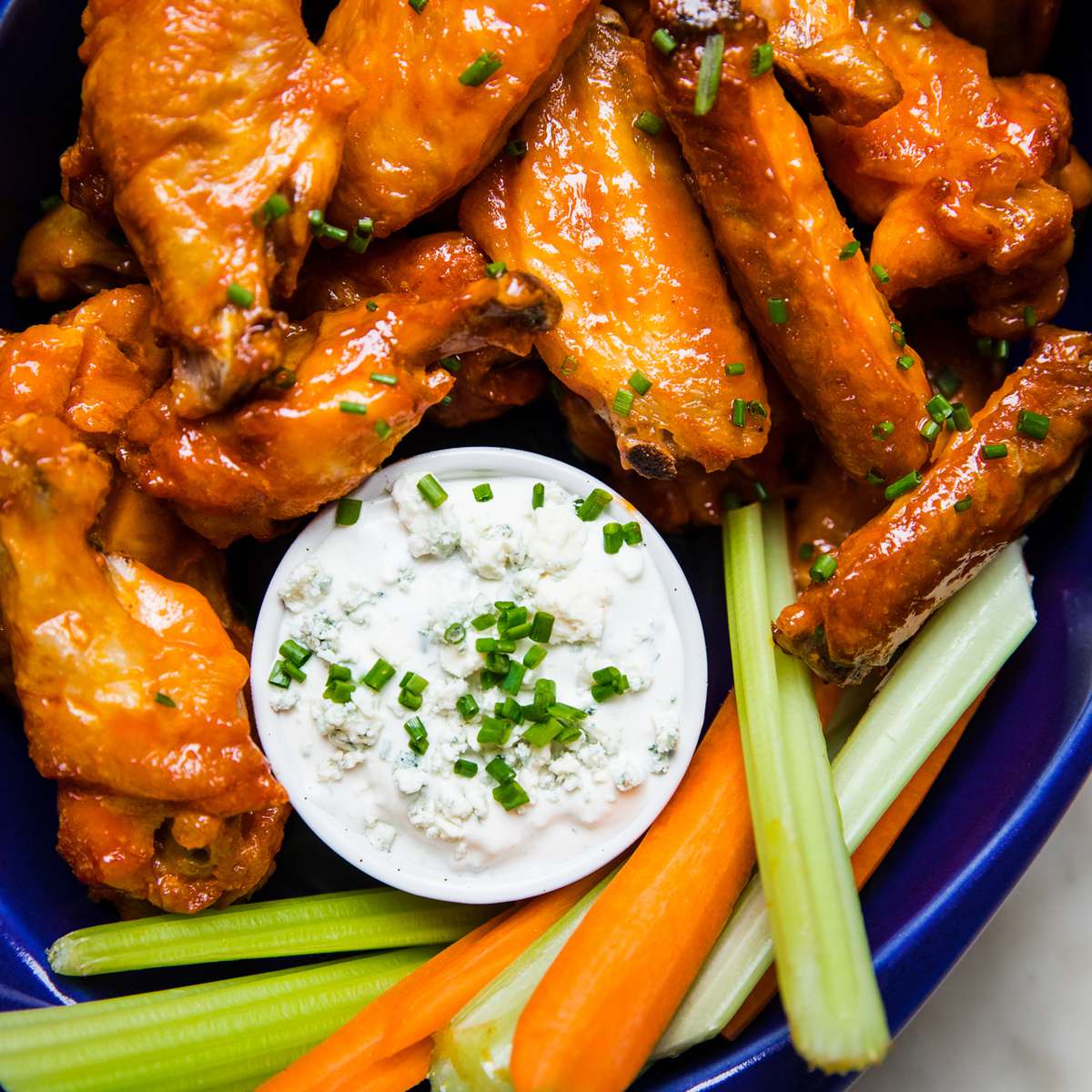 Plate of baked buffalo chicken wings served with fresh celery sticks, carrot sticks, and blue cheese dressing for dipping