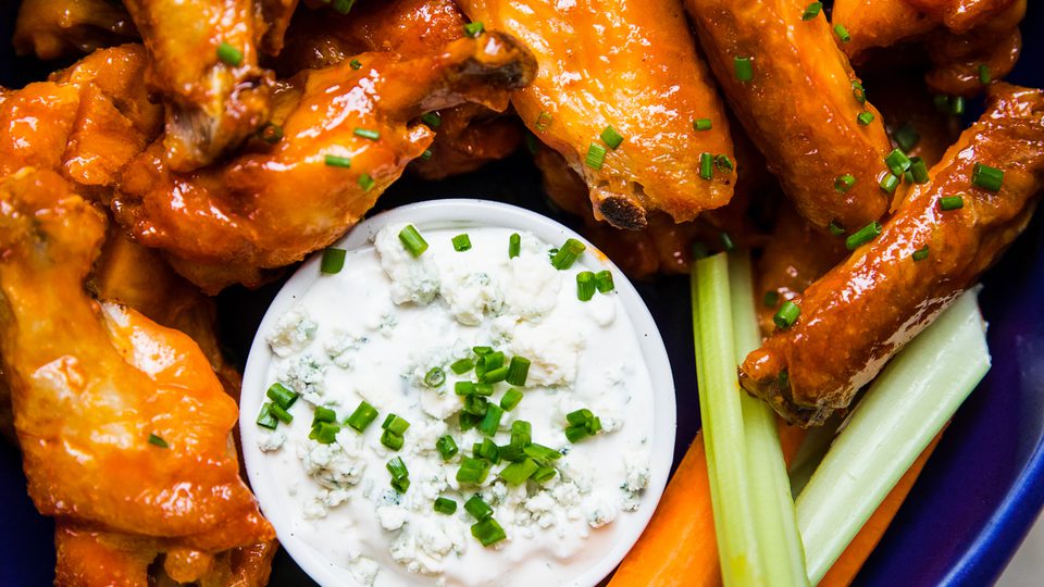 Plate of baked buffalo chicken wings served with fresh celery sticks, carrot sticks, and blue cheese dressing for dipping