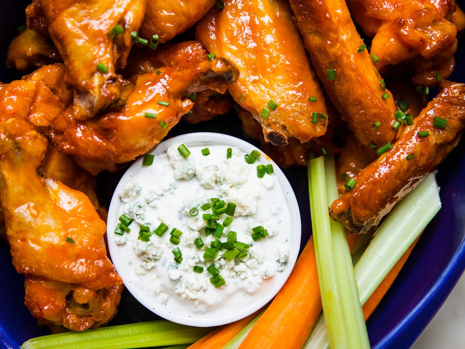 Plate of baked buffalo chicken wings served with fresh celery sticks, carrot sticks, and blue cheese dressing for dipping