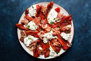 Burrata with Roasted Red Peppers, Prosciutto, olive oil and fresh parsley on a plate