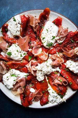 Burrata with Roasted Red Peppers, Prosciutto, olive oil and fresh parsley on a plate