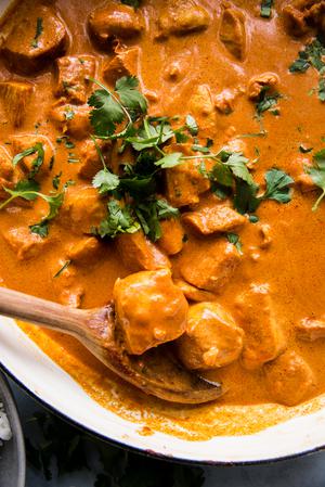 a pot of butter chicken topped with fresh cilantro being stirred with a wooden spoon