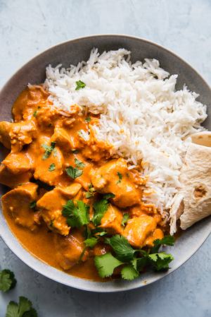a bowl of Butter chicken on top of white rice topped with cilantro and served with naan