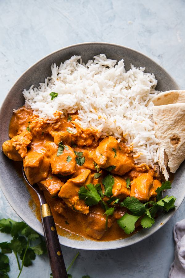 homemade butter chicken in a bowl served with rice, naan and cilantro