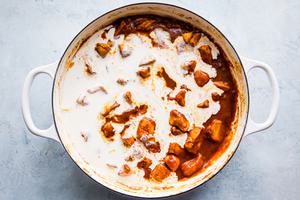 heavy cream being added to butter chicken in a large white pot