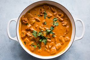 a pot of butter chicken topped with fresh cilantro being stirred with a wooden spoon
