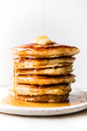 stack of buttermilk pancakes topped with butter and dripping with syrup