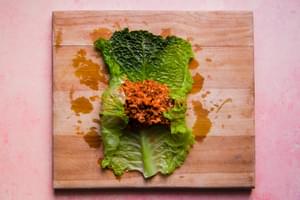 a boiled cabbage leaf being filled and rolled with a ground beef, sausage and rice mixture
