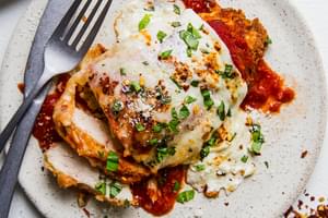 homemade chicken parmesan on a plate with marinara, basil and fresh mozzarella with a fork and knife