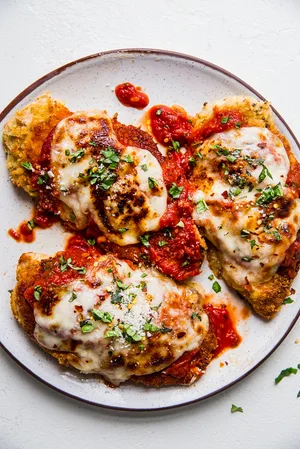 homemade chicken parmesan on a plate with marinara, basil and fresh mozzarella