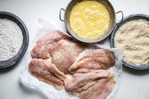 beaten eggs, flour, panko, bread crumbs, and chicken breasts seasoned with salt and pepper in bowls to bread the chicken