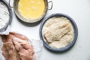 beaten eggs, flour, panko, bread crumbs, and chicken breasts seasoned with salt and pepper in bowls to bread the chicken