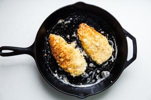 2 breaded chicken filets in a skillet frying in olive oil
