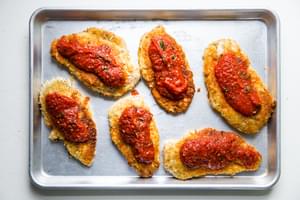pan fried breaded chicken breast on a baking sheet topped with marinara